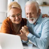 Uśmiechnięta para seniorów korzystająca z laptopa.
